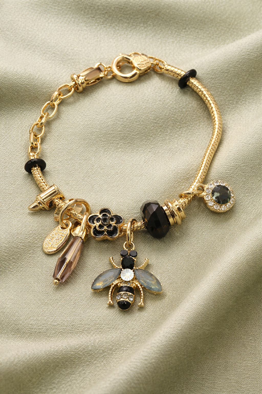 Anti-Tarnish, Ashaarya, Ashaarya Jewels, Ashaarya Jewellery, Gold bracelet with various charms on a beige fabric background