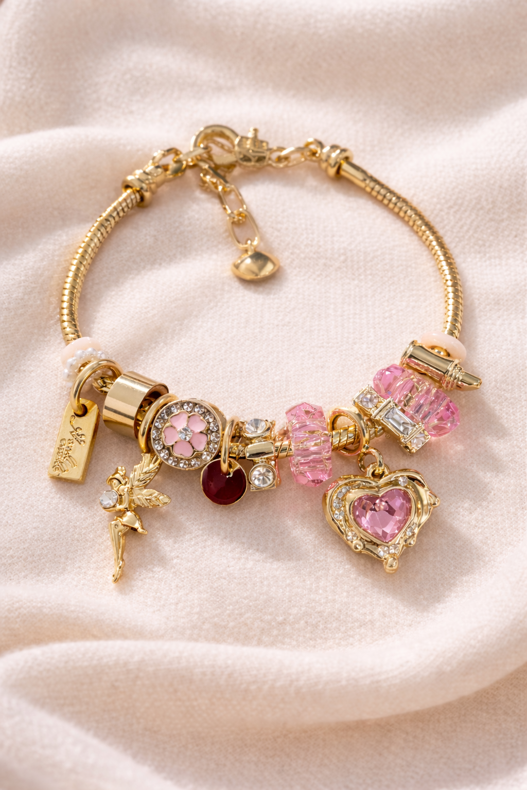 Gold Charm bracelet with pink and gold charms on a light pink background