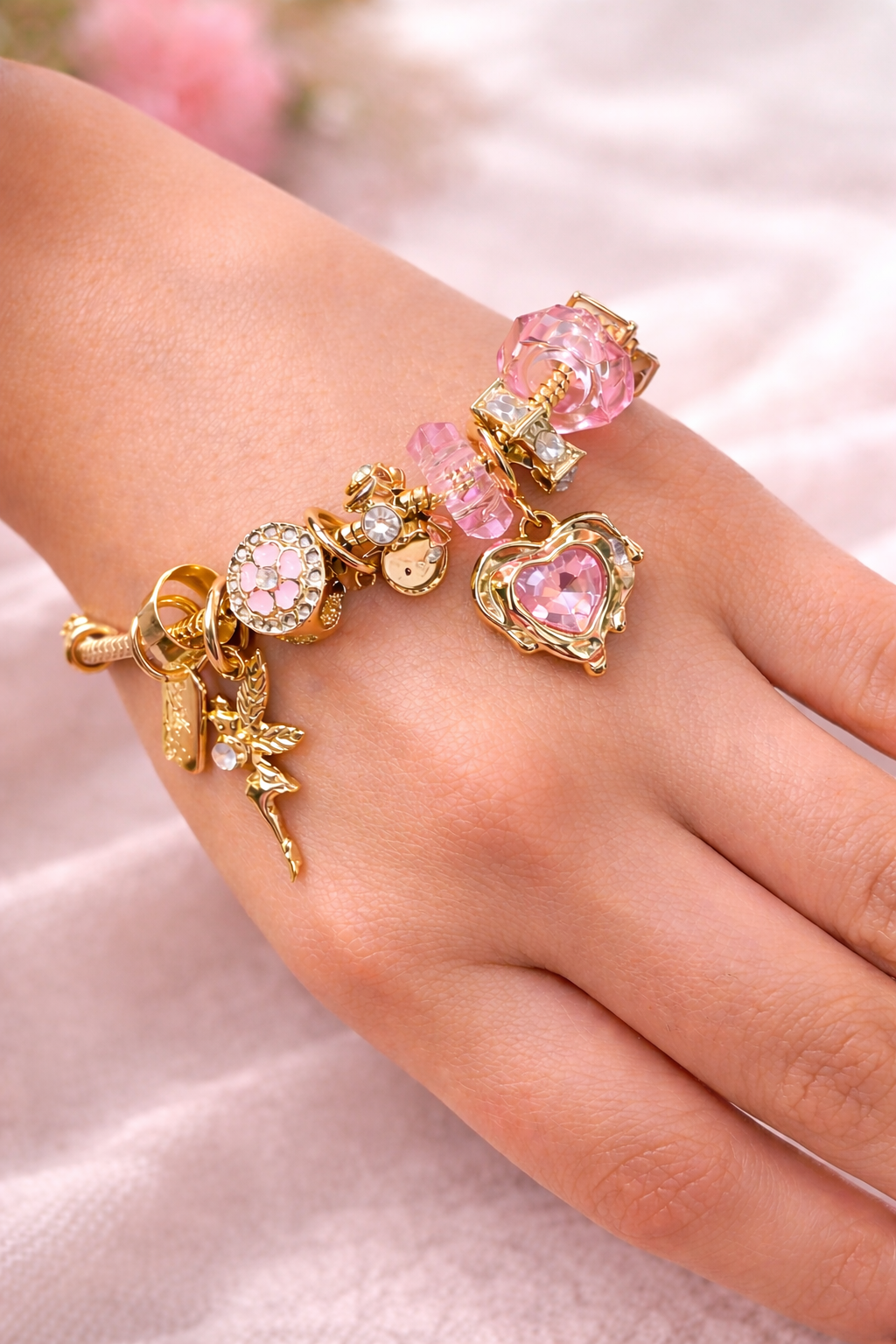 Hand wearing a gold bracelet with pink heart charm on a soft pink background