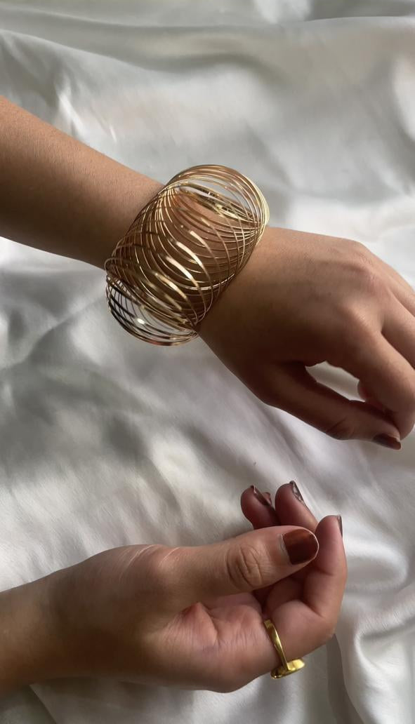 Close-up of a hand wearing a gold bracelet on a white fabric background