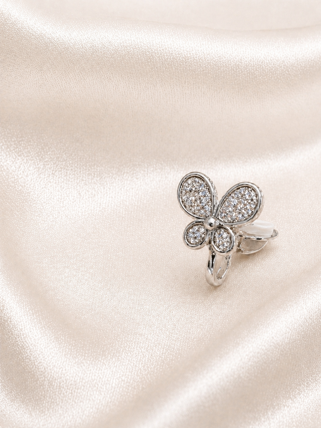 Silver butterfly-shaped earring with clear stones on a satin surface.Elegant butterfly earrings with smooth single diamonds anti-tarnish comfort jewellery for sensitive ears