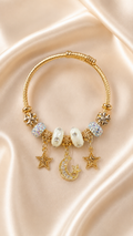 Gold bracelet with star, moon, and pearl charms on a beige fabric background