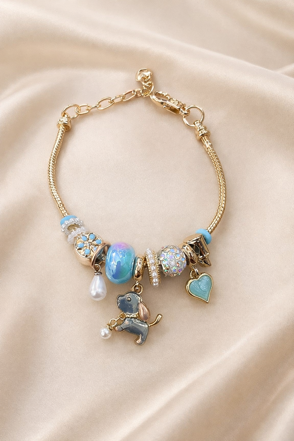 Anti-tarnish aqua charm bracelet with dog pendant and heart charm on gold snake chain – comfort jewellery by Ashaarya. Gold bracelet with various charms on a beige fabric background
