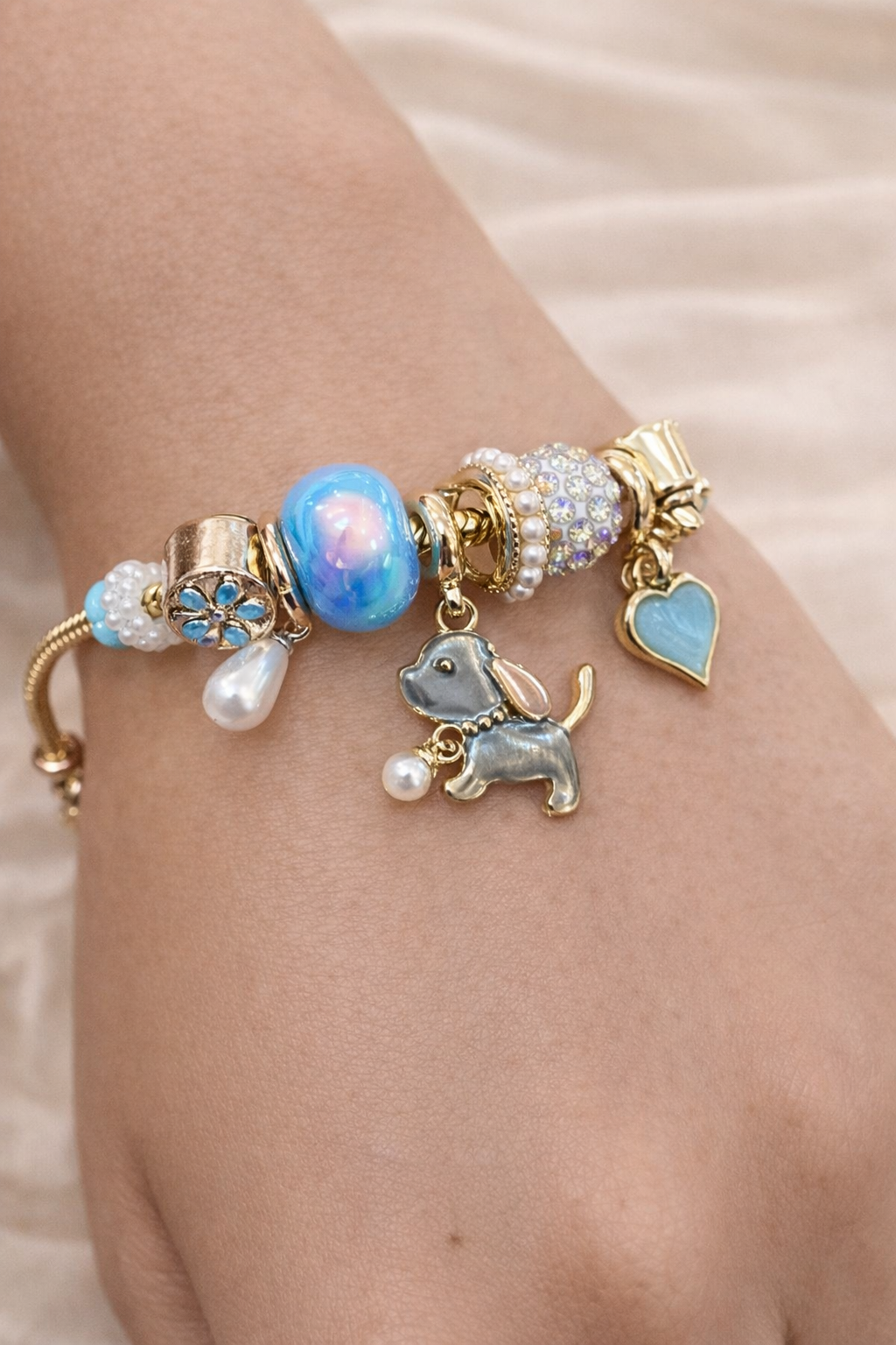 Anti-tarnish aqua charm bracelet with dog pendant and heart charm on gold snake chain – comfort jewellery by Ashaarya. Bracelet with various charms including a dog, pearl, and heart on a wrist.
