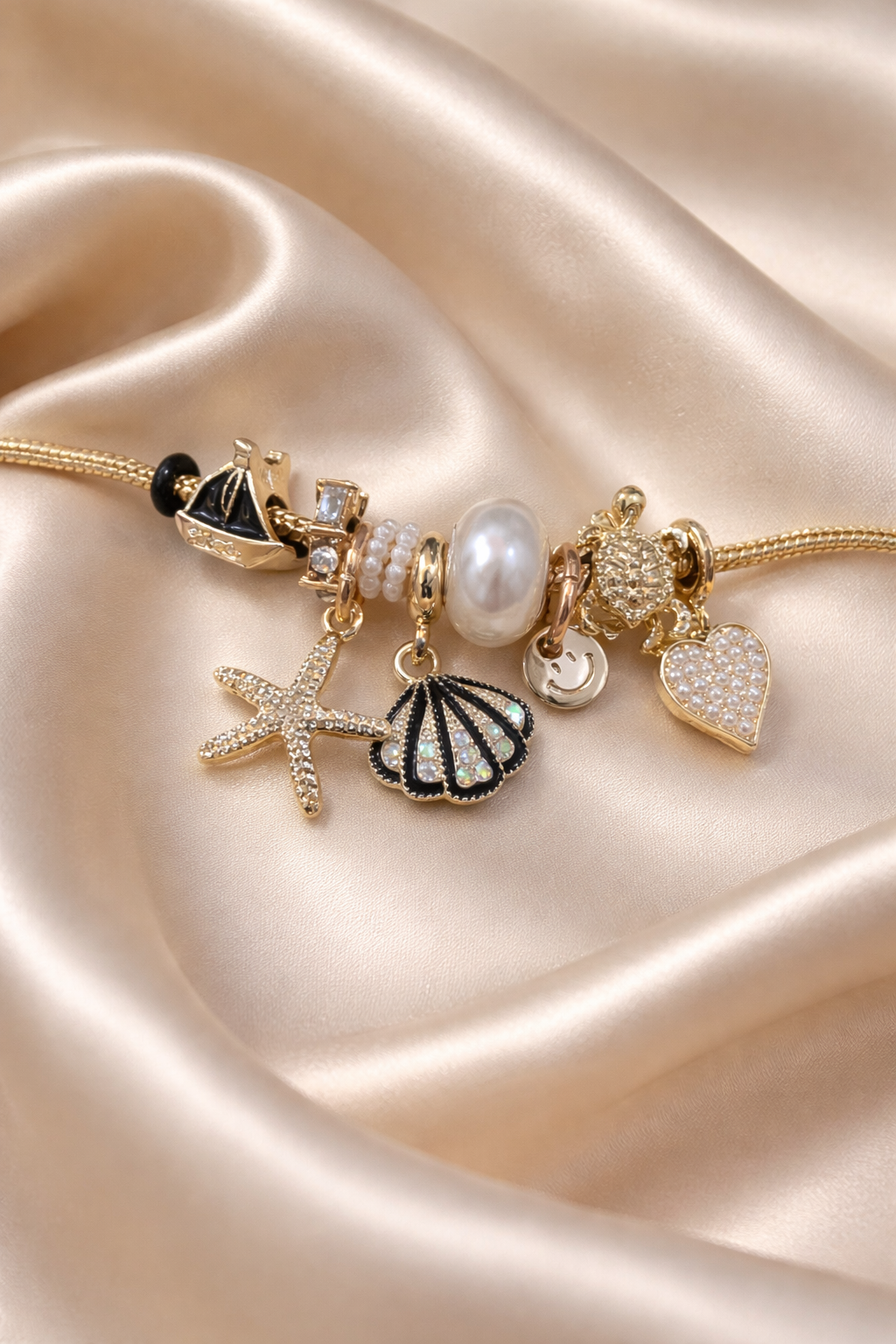 Anti-tarnish ocean charm bracelet with pearl, shell and starfish charms on gold snake chain – comfort jewellery by Ashaarya, Gold bracelet with various charms on a satin surface