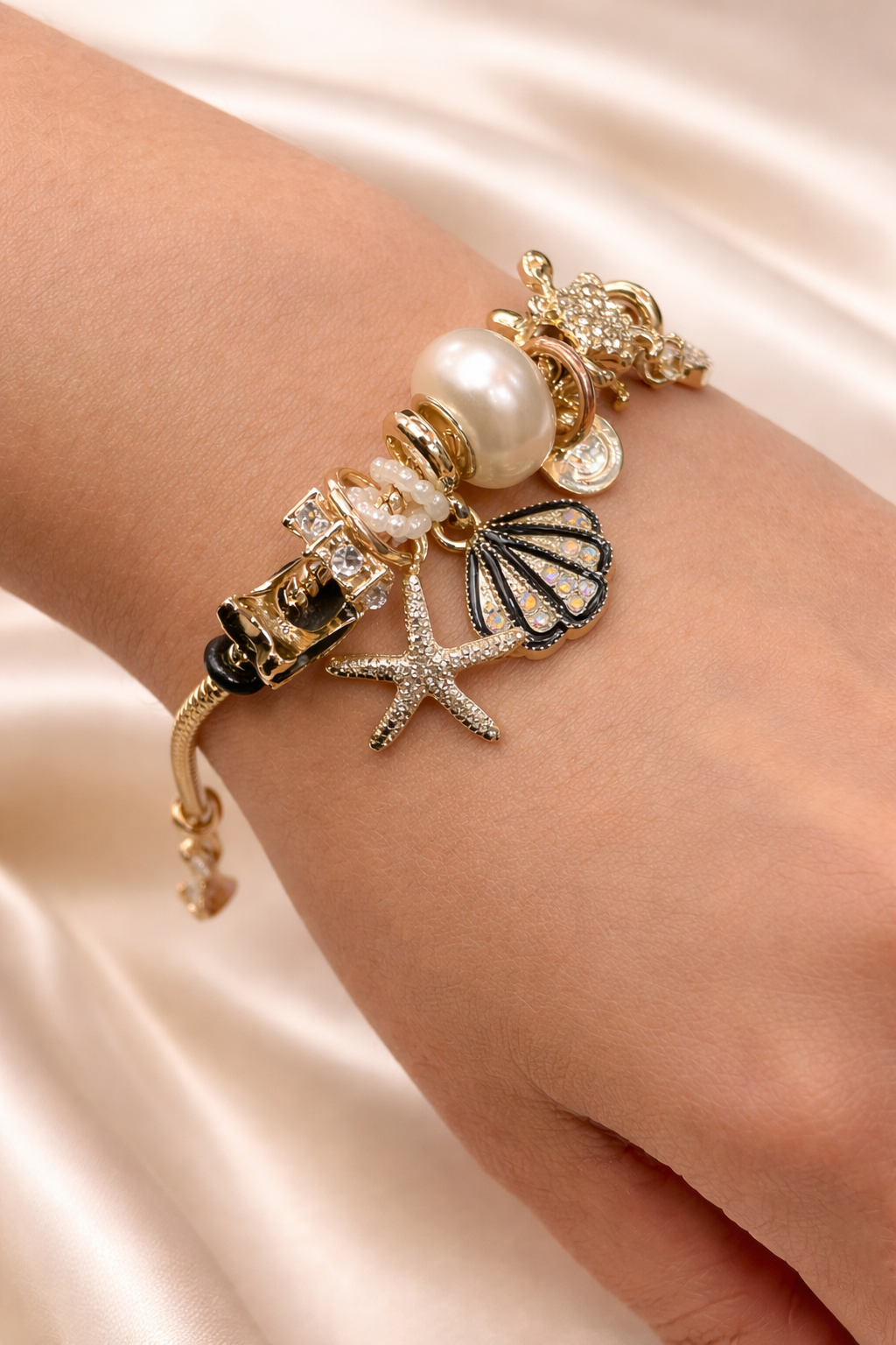 Anti-tarnish ocean charm bracelet with pearl, shell and starfish charms on gold snake chain – comfort jewellery by Ashaarya, Bracelet with starfish, shell, and pearl charm on a wrist against a satin background