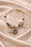 Anti-tarnish ocean charm bracelet with pearl, shell and starfish charms on gold snake chain – comfort jewellery by Ashaarya. Gold bracelet with various charms on a satin surface