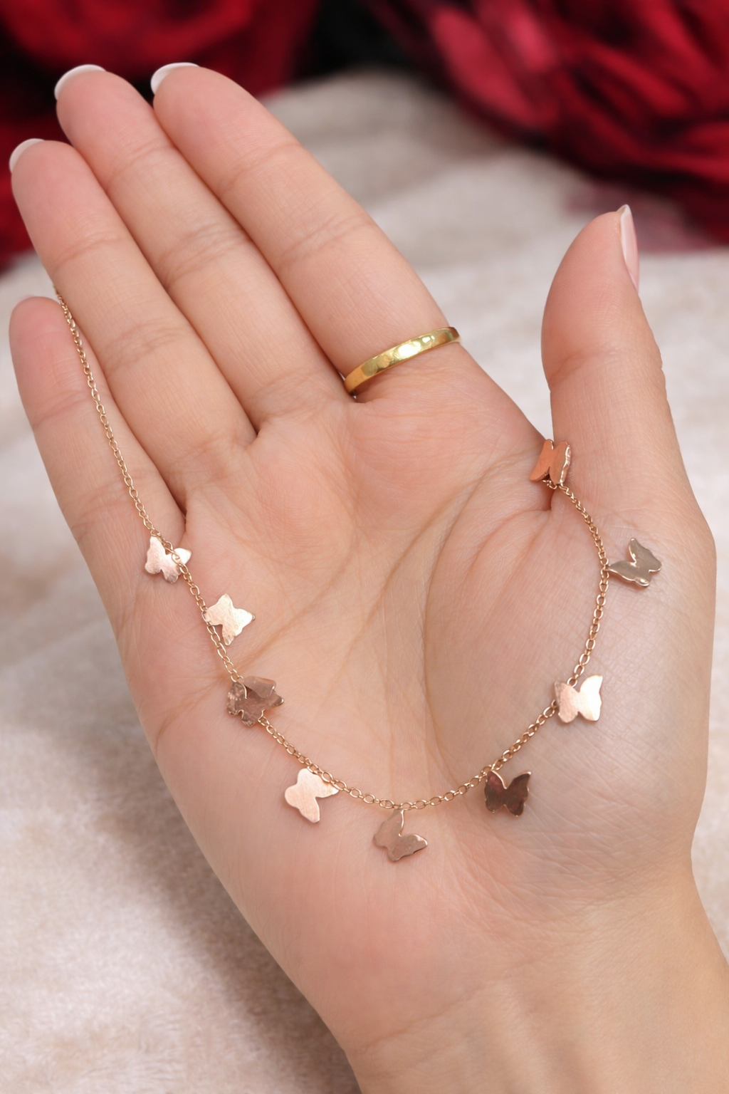 Anti Tarnish necklace, charm bracelets, ashaarya, ashaarya jewels, ashaarya jewellery, Rose gold butterfly necklace on a hand with a blurred red background