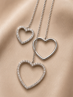 Three silver heart-shaped pendants on a beige fabric background. 925 sterling silver earrings, sterling silver heart studs, silver heart earrings, 925 silver earrings for women, heart stud earrings, cubic zirconia earrings, hypoallergenic earrings, everyday silver jewellery, sterling silver studs, dainty silver earrings, silver jewellery India, Ashaarya
