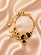 Black Diva anti-tarnish charm bracelet with black crystal heart charm and gold-tone finish. Gold bracelet with black heart charms on a pink satin background