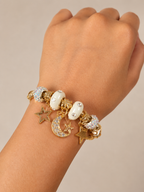 Gold bracelet with star, moon, and heart charms on a wrist against a beige background