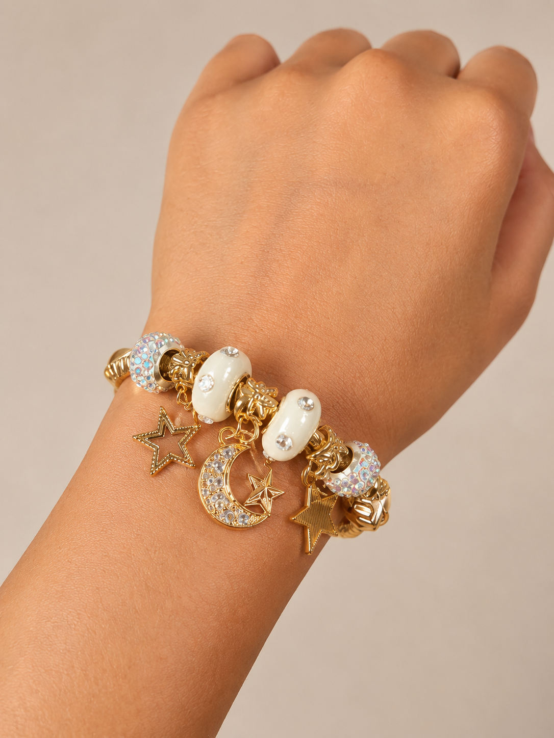 Gold bracelet with star, moon, and heart charms on a wrist against a beige background