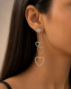 Close-up of a woman wearing heart-shaped earrings with a neutral background. 925 sterling silver earrings, sterling silver heart studs, silver heart earrings, 925 silver earrings for women, heart stud earrings, cubic zirconia earrings, hypoallergenic earrings, everyday silver jewellery, sterling silver studs, dainty silver earrings, silver jewellery India, Ashaarya